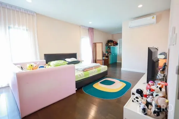 Detached House for rent or sale in Lam Luk Ka, Pathum Thani - Spacious master bedroom with double bed, sofa, TV unit and wood flooring.
