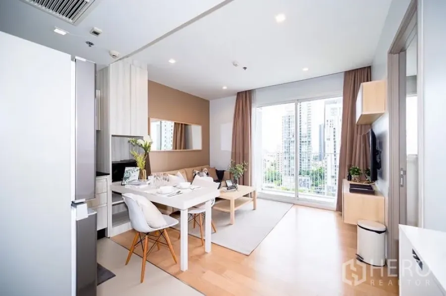 Condominium for rent or sale in Watthana, Bangkok - Bright open-plan living and dining area with kitchenette, balcony doors, and Bangkok city view in a Thonglor condo.