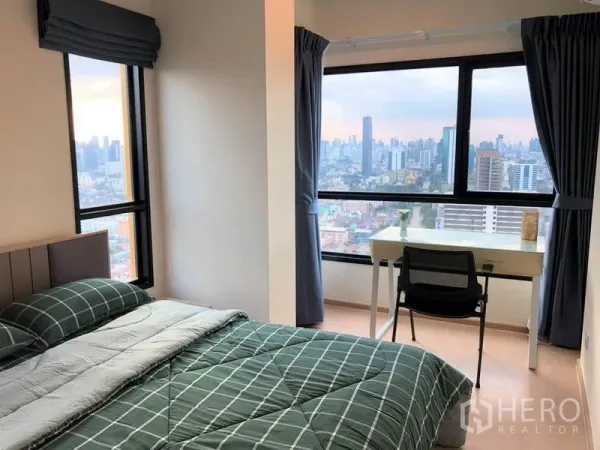 คอนโด ขายในSuan Luang, Bangkok - ห้องนอนมุมอาคาร หน้าต่างบานใหญ่ โต๊ะทำงาน มองเห็นสกายไลน์กรุงเทพฯ ยามเย็น