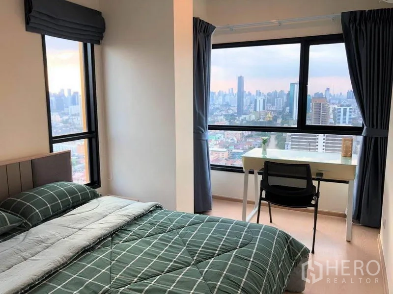 คอนโด ขายในSuan Luang, Bangkok - ห้องนอนมุมอาคาร หน้าต่างบานใหญ่ โต๊ะทำงาน มองเห็นสกายไลน์กรุงเทพฯ ยามเย็น