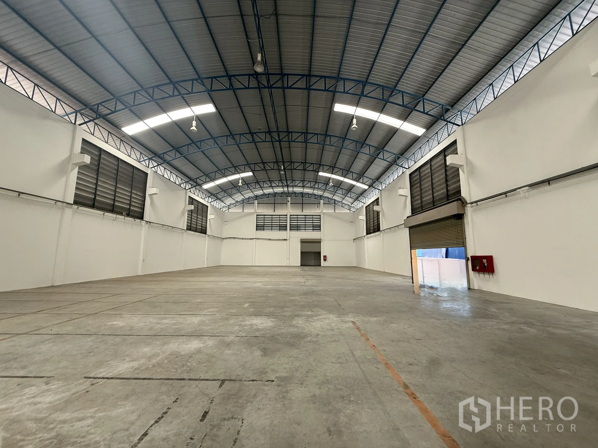 Warehouse for rent or sale in Bang Bo, Samut Prakan - Open warehouse floor with an opened roller shutter and fire safety equipment on the wall.