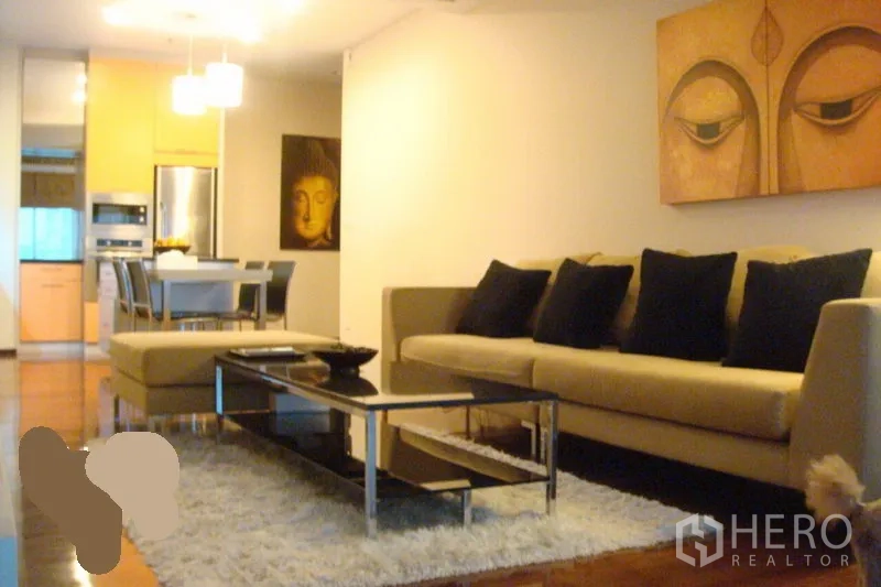 Condominium for rent in Watthana, Bangkok - Bright living room with beige sofa, black cushions, glass coffee table on a shag rug, open to dining and kitchen with warm wood floors and pendant lights.