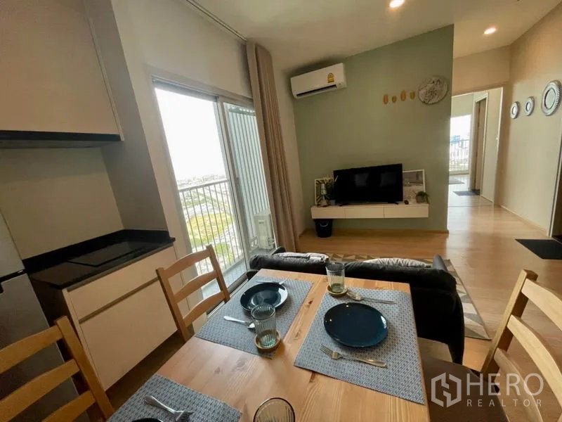 Condominium for rent in Huai Khwang, Bangkok - Open-plan kitchen and dining facing living area with TV and balcony.