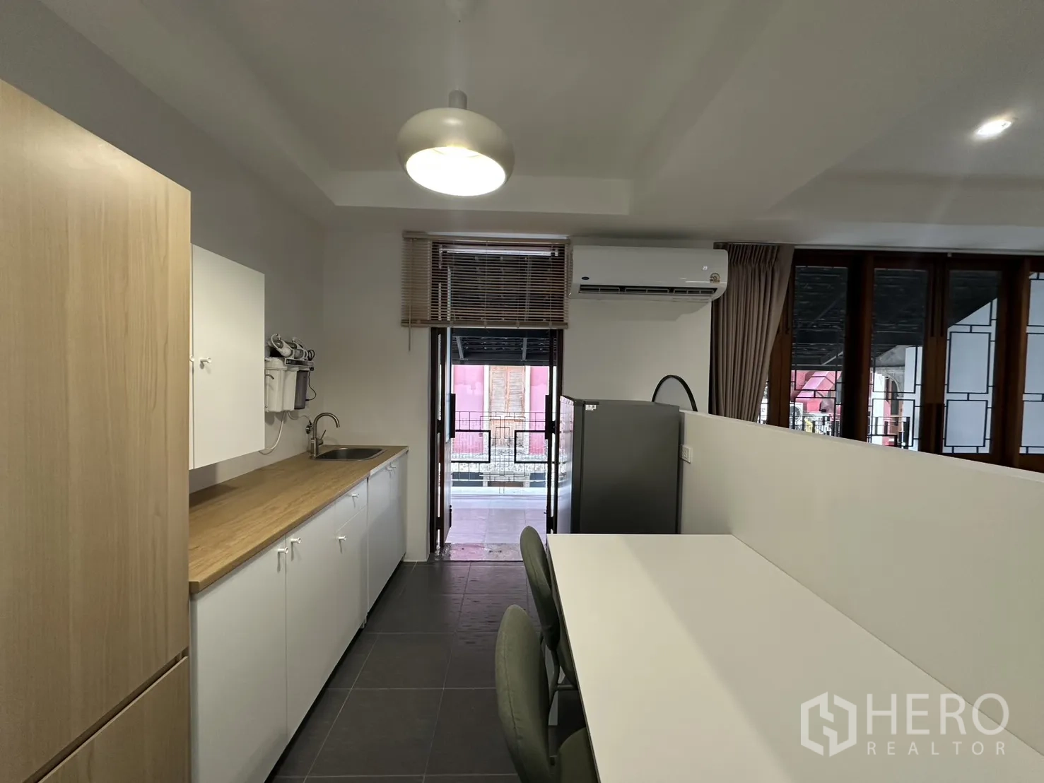 Apartment for rent in Pathum Wan, Bangkok - Kitchen and dining area with long counter, table, refrigerator, and air conditioner.