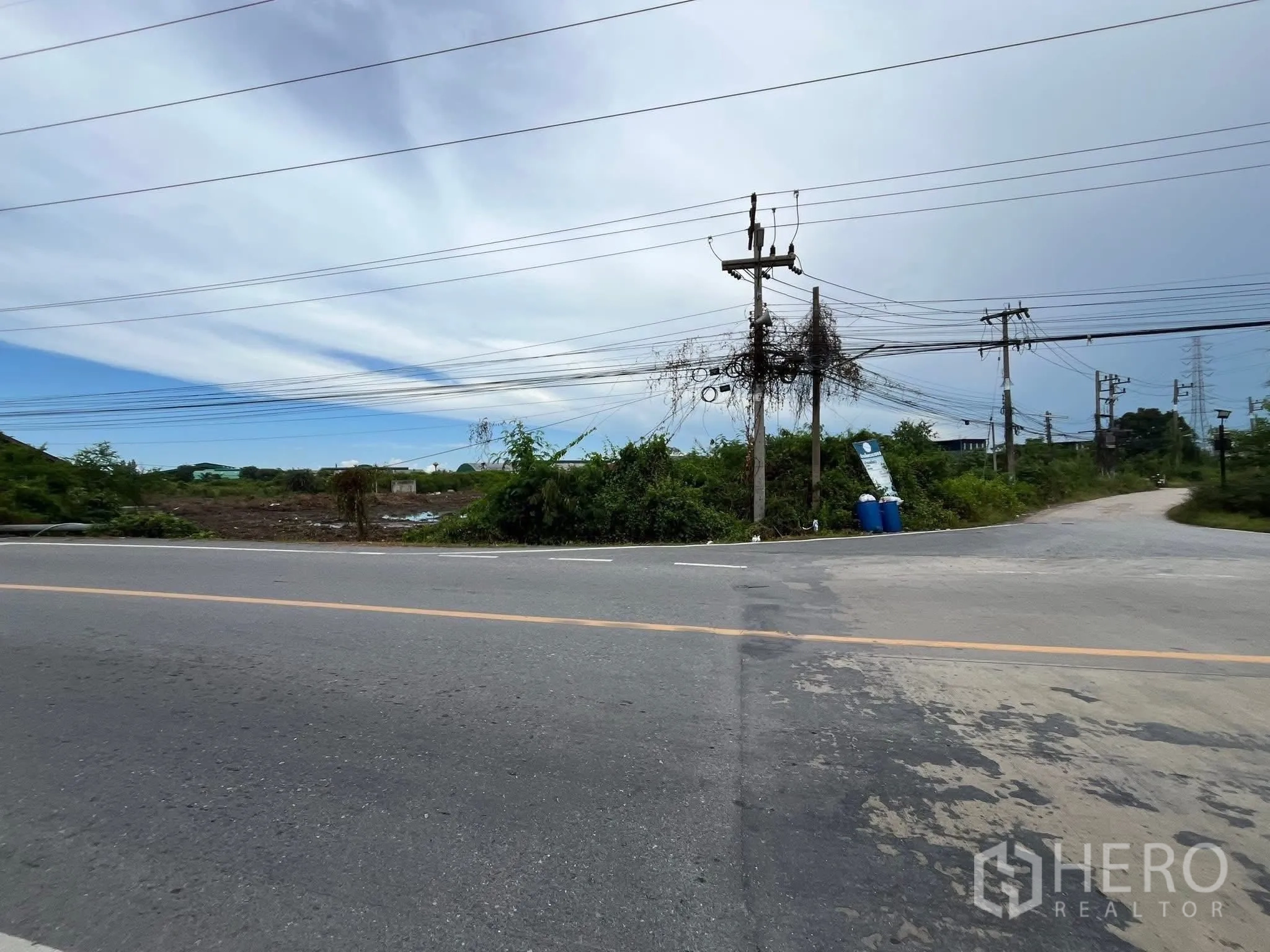 Land for sale in Mueang Samut Sakhon, Samut Sakhon - Corner paved road with power poles and access to a cleared land plot.