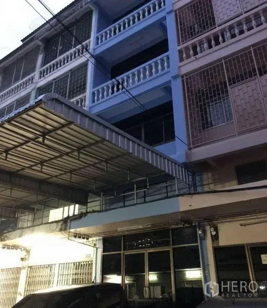 店屋 出租在Khlong Toei, Bangkok - 傍晚视角的店屋正面，蓝色外墙、栏杆阳台与大型钢雨棚。