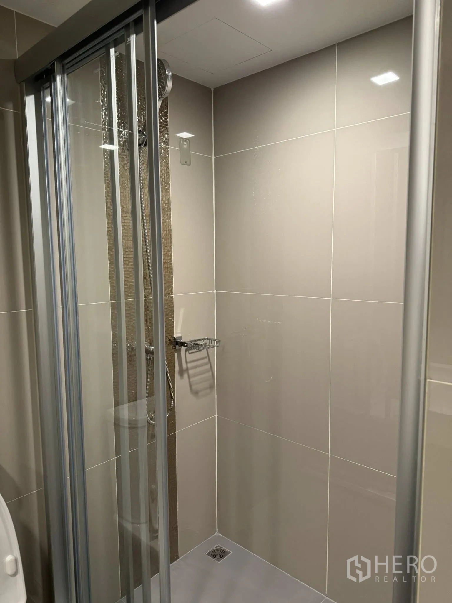 Condominium for rent in Huai Khwang, Bangkok - Clean bathroom with tiled walls and a glass-enclosed shower with handheld showerhead.