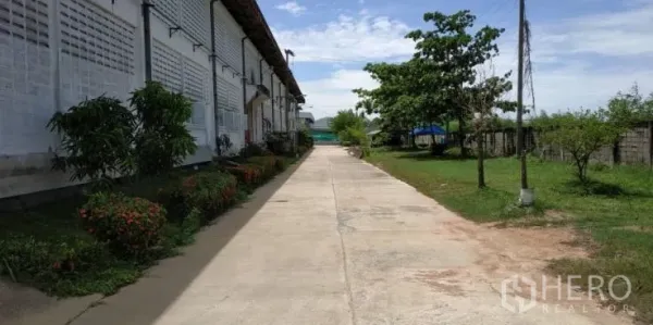 Factory for rent in Chachoengsao - Concrete walkway with landscaping and trees along the side of the factory building.