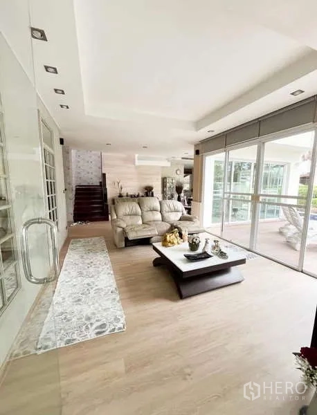 Detached House for rent in Bang Phli, Samut Prakan - Airy living room with floor-to-ceiling sliding glass, light wood floors, sofa set and staircase.