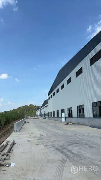 คลังสินค้า ให้เช่าในBan Bueng, Chon Buri - มุมมองด้านข้างของโกดังสีขาวสมัยใหม่ ทางวิ่งยาวและภูเขาเตี้ยด้านหลัง