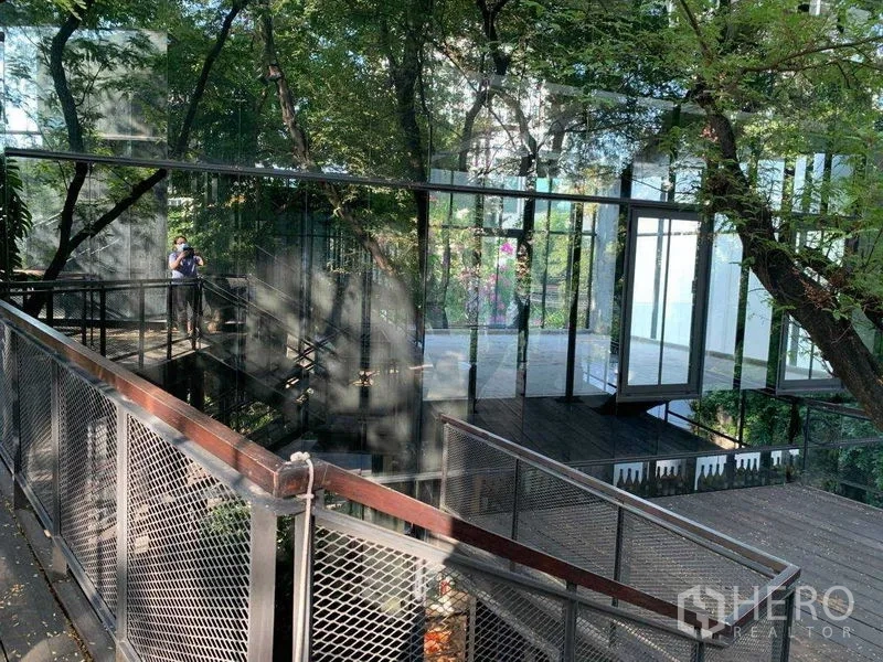 办公空间 出租在Khlong Toei, Bangkok - 被大树环绕的玻璃建筑与金属栈道的高架连桥。