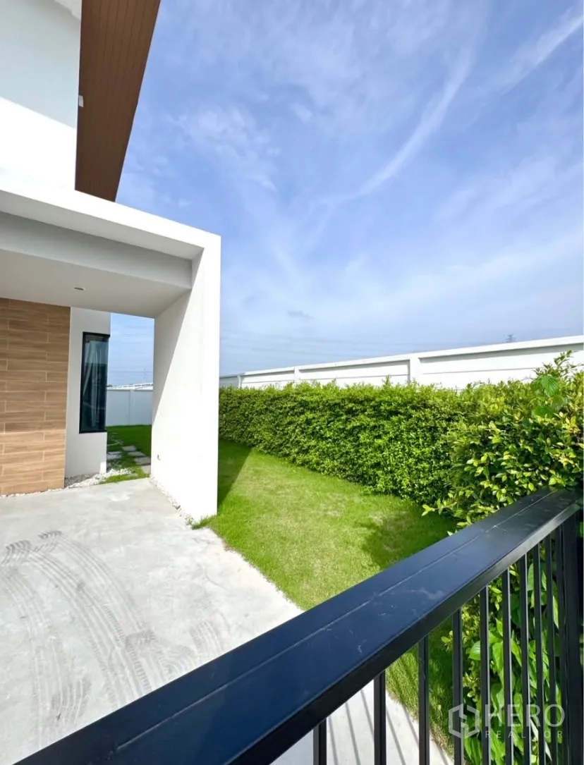 Detached House for rent in Samut Prakan - Side yard with green lawn, trimmed hedge and a covered carport beside the house.