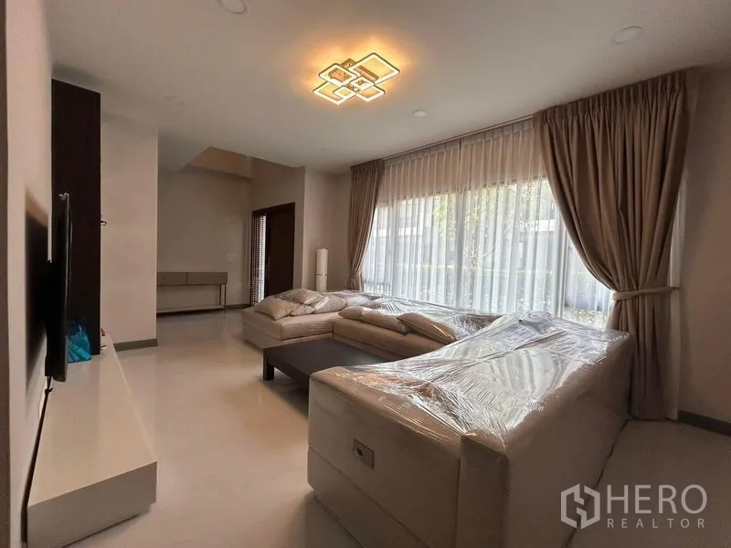 บ้าน ให้เช่า - ห้องนั่งเล่นกว้าง โซฟามุม ผ้าม่านโปร่ง และโคมไฟเพดาน