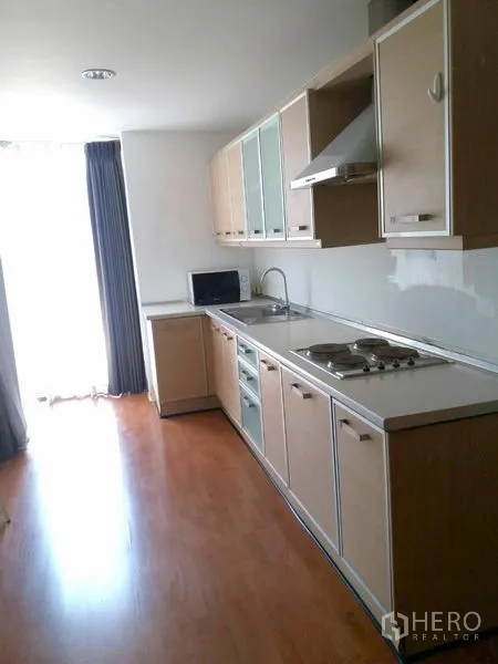 คอนโด ให้เช่าในWatthana, Bangkok - ครัวแบบแกลลีย์สว่าง พร้อมท็อปยาว ตู้ลายไม้ เตาและเครื่องดูดควัน ใกล้ประตูหน้าต่าง.