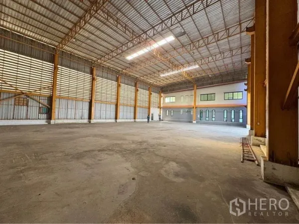 Warehouse for rent or sale in Mueang Samut Sakhon, Samut Sakhon - Spacious warehouse floor with steel trusses, skylight panels, and an attached office block with windows.