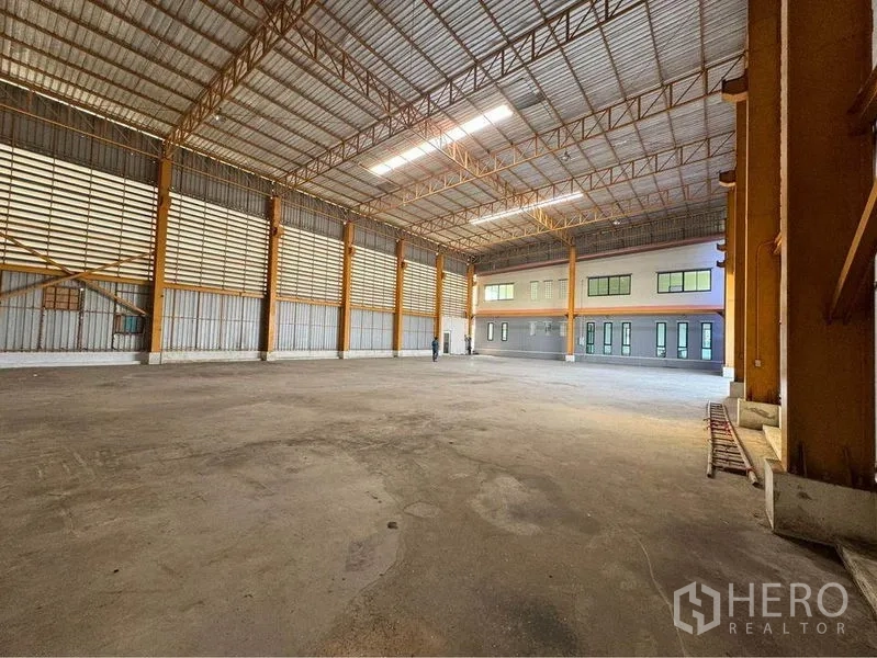 Warehouse for rent or sale in Mueang Samut Sakhon, Samut Sakhon - Spacious warehouse floor with steel trusses, skylight panels, and an attached office block with windows.
