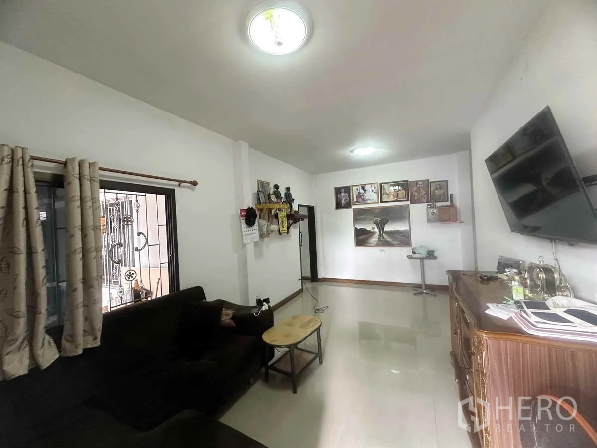 独立式住宅 出售在Pathum Thani - 客厅另一视角，沙发、电视与墙面装饰画。