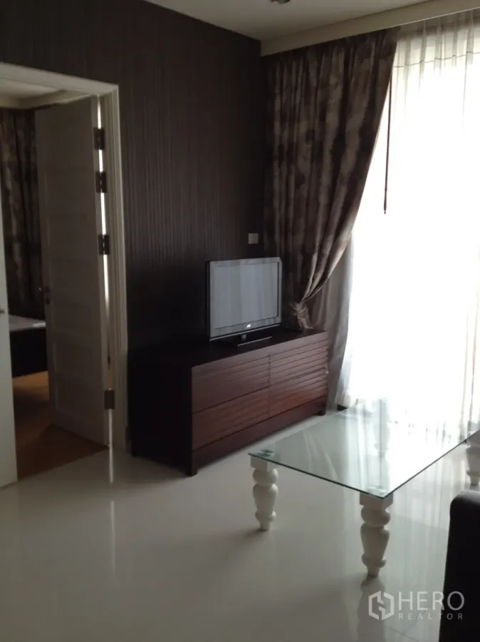 公寓 出租在Khlong Toei, Bangkok - 客厅采光充足，设电视柜、玻璃茶几与落地窗帘。