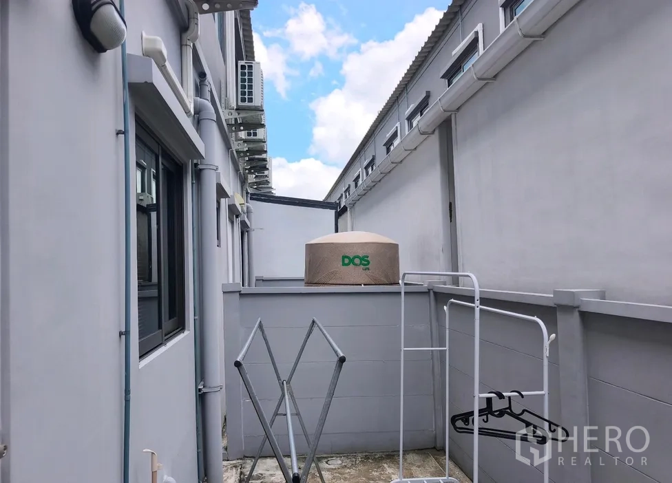 Townhouse for rent in Bang Phli, Samut Prakan - Narrow service yard with water tank, clothes-drying racks and exterior air-conditioning units.