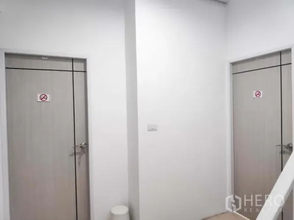 Home Office for rent in Khlong Toei, Bangkok - Hallway with two light-wood doors and white walls, suitable for separate restrooms or storage.