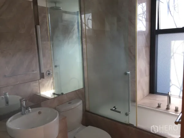 Condominium for rent in Sathon, Bangkok - Modern bathroom with bathtub, glass shower enclosure, and marble-look tiles.
