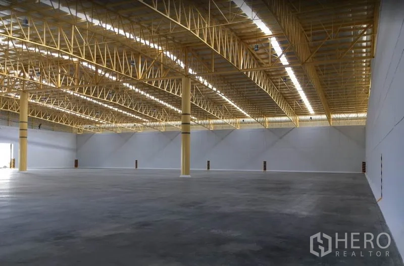 Warehouse for rent in Phra Nakhon Si Ayutthaya - Spacious warehouse interior with yellow steel truss roof, skylight strips, and polished concrete floor.