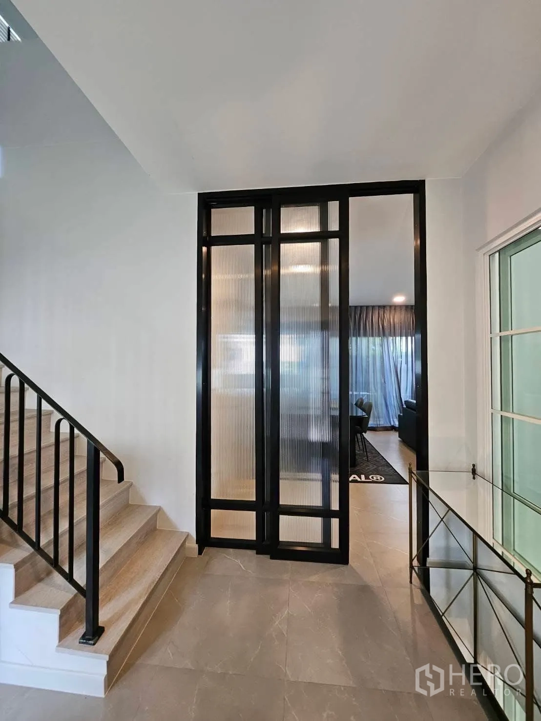 บ้านเดี่ยว for rent in Bang Phli, Samut Prakan - โถงบันไดพื้นไม้ราวเหล็ก ข้างประตูกระจกกรอบดำแบบลูกฟูก เชื่อมต่อสู่ห้องนั่งเล่น