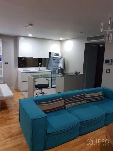 Condominium for sale in Bang Rak, Bangkok - View of living room to sleek kitchen island and appliances on wood floors.