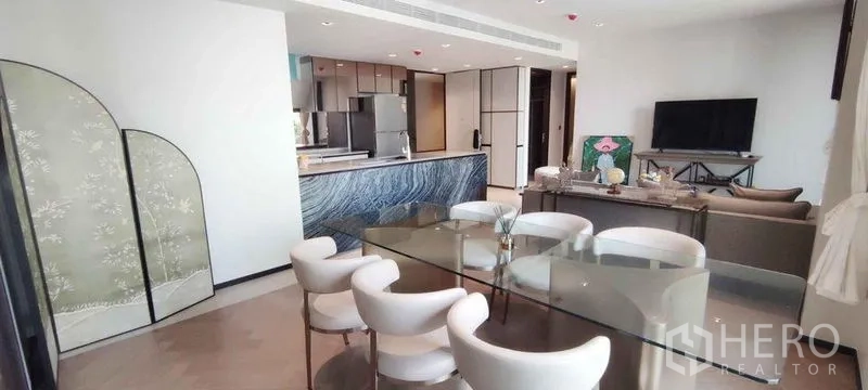 คอนโด ให้เช่าในWatthana, Bangkok - พื้นที่นั่งเล่น-ทานอาหารแบบโอเพนแปลน โต๊ะกระจก เก้าอี้สีขาว และเคาน์เตอร์ครัวหินลายสีน้ำเงิน