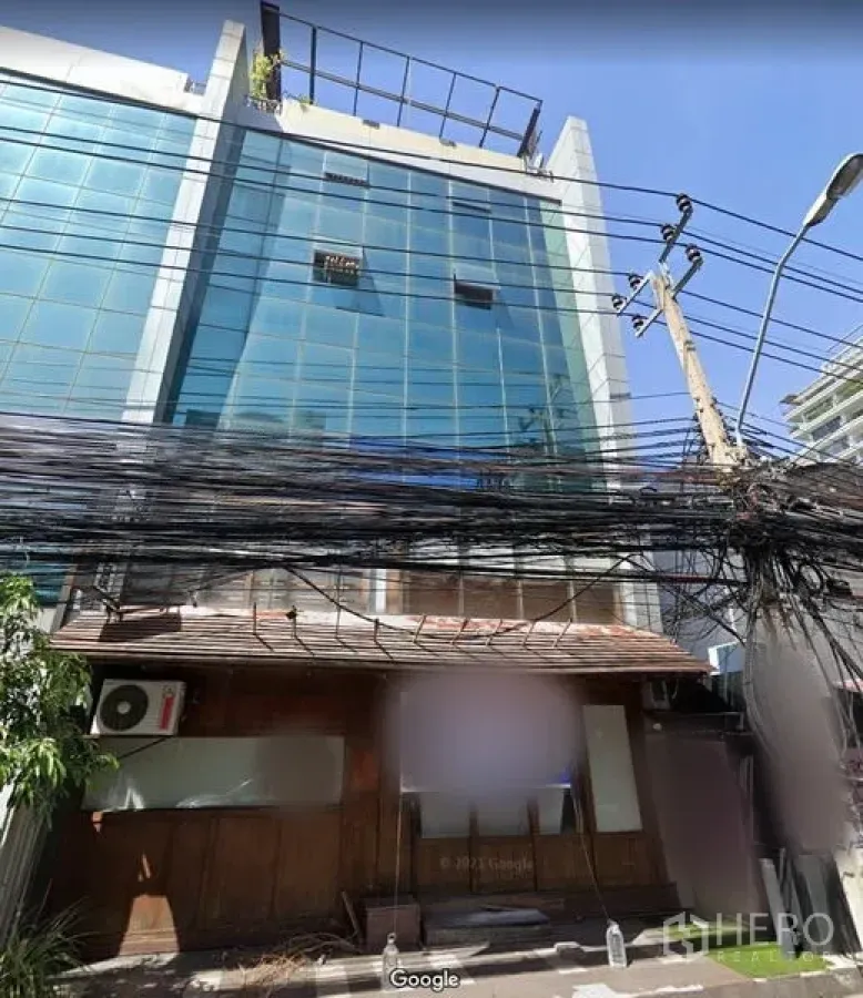 零售空间 出租在Khlong Toei, Bangkok - Thonglor 商圈玻璃写字楼下方的街边木质店面立面，前方可见电线与电线杆。