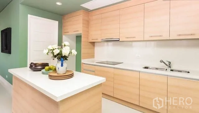 Condominium for rent or sale in Khlong Toei, Bangkok - Light wood kitchen with white island, induction hob, and built-in cabinets.
