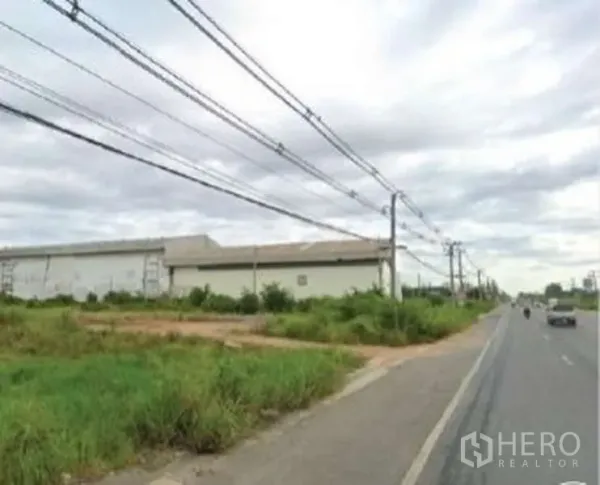 Land for sale in Chachoengsao - Vacant plot next to a large warehouse along a dual carriageway lined with power poles.