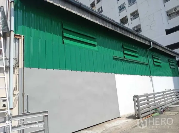 Warehouse for rent in Suan Luang, Bangkok - Exterior side wall of a green and white metal-clad warehouse with louvered vents and fence.