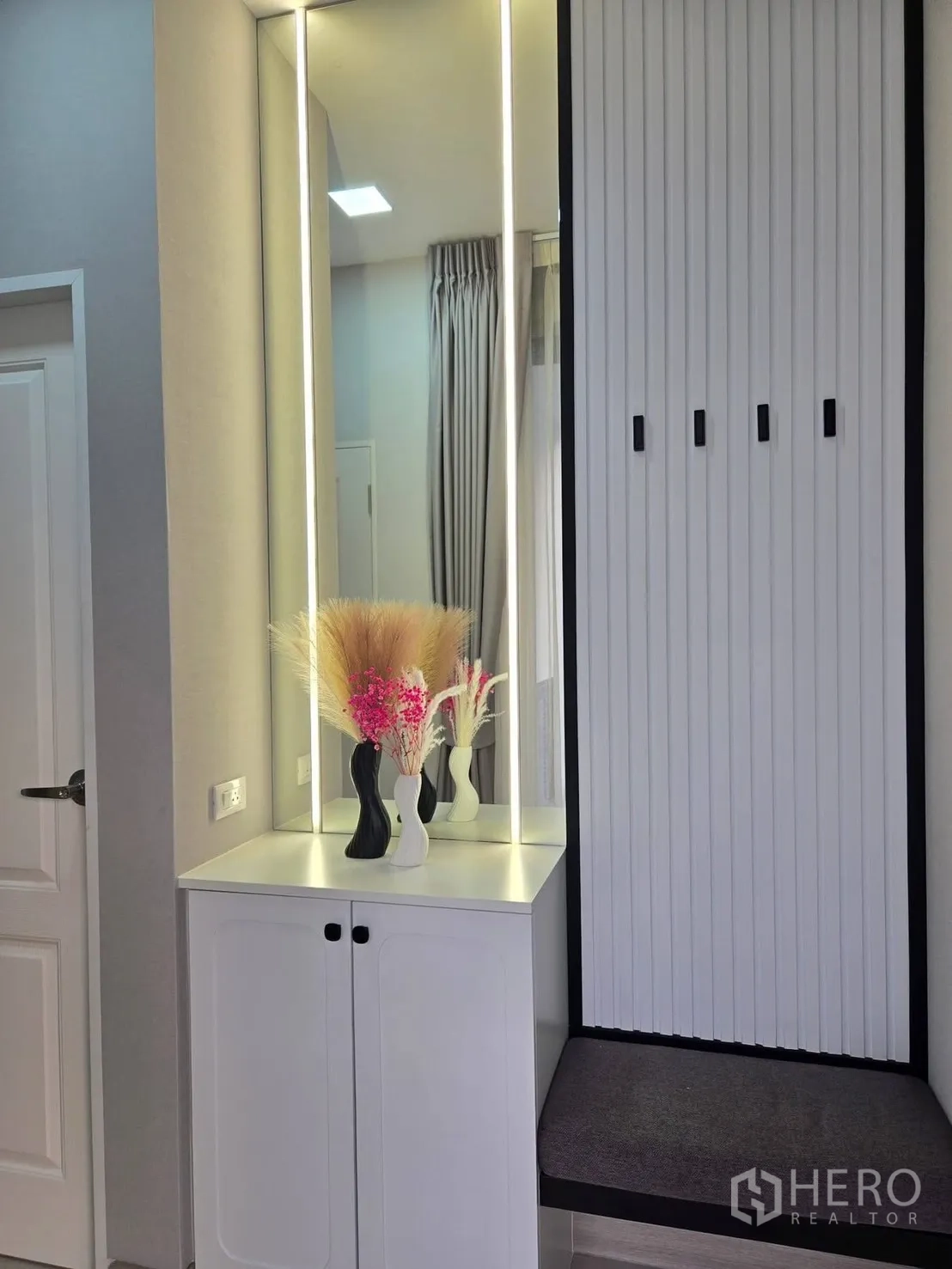 Detached House for rent or sale in Bang Phli, Samut Prakan - Built-in entry console with illuminated mirror, cabinet, and bench with slatted wall and dried flower vases.
