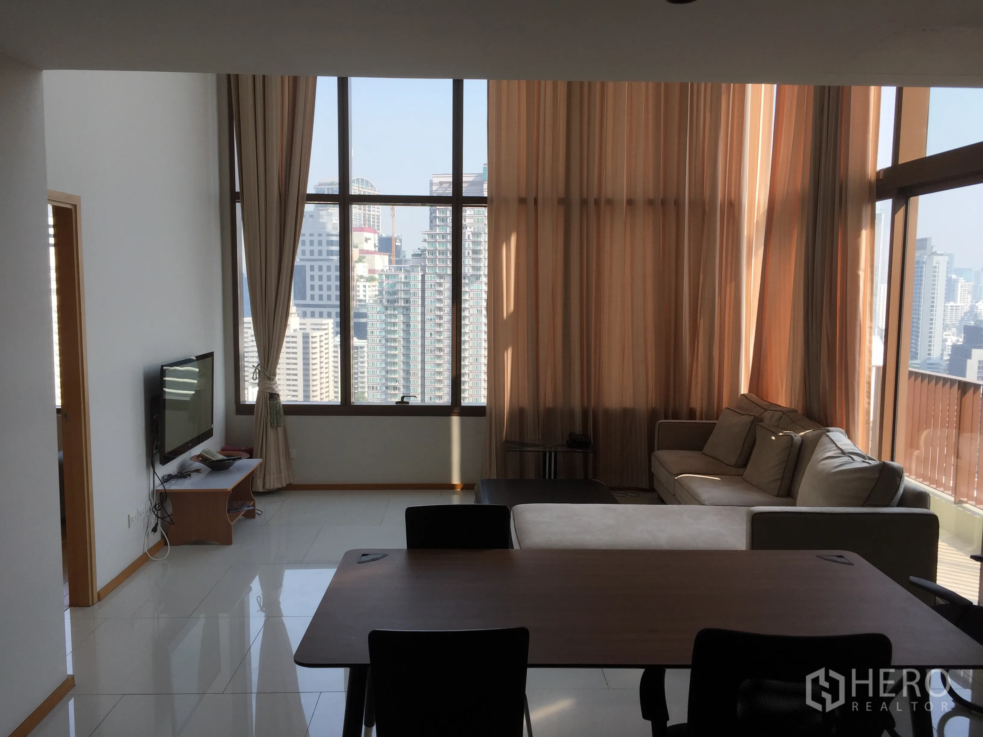 คอนโด ให้เช่าหรือขายในKhlong Toei, Bangkok - ห้องนั่งเล่นหน้าต่างสูงจรดเพดาน เห็นวิวสกายไลน์ พร้อมโซฟาและโต๊ะทานข้าว