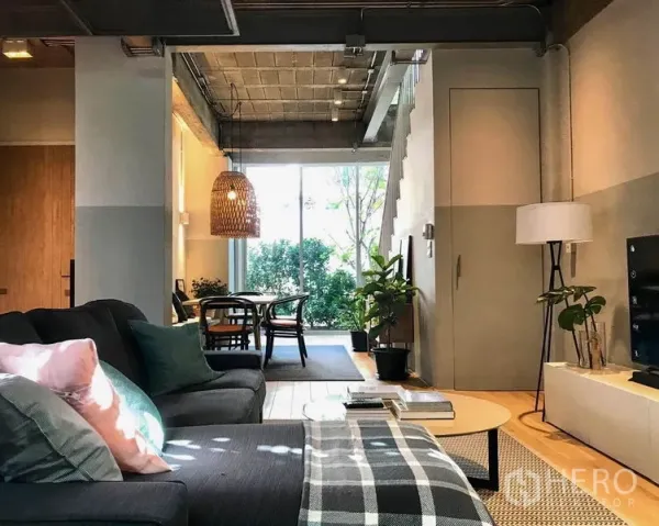 Townhouse for rent in Khlong Toei, Bangkok - Cozy living room facing the dining zone with concrete ceiling and full-height window to leafy views.