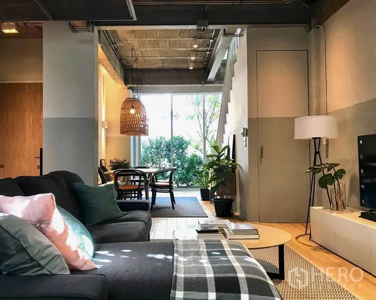 Townhouse for rent in Khlong Toei, Bangkok - Cozy living room facing the dining zone with concrete ceiling and full-height window to leafy views.