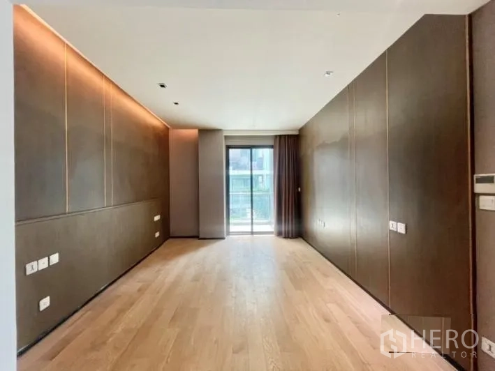 Detached House for rent or sale in Khlong Toei, Bangkok - Bedroom with warm wood floors, dark accent walls and a sliding door to a balcony.