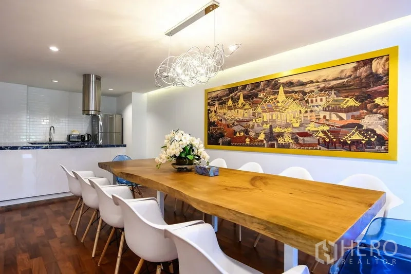 Condominium for rent in Pathum Wan, Bangkok - Dining room with a long live-edge wooden table, white chairs, and an open kitchen with a stainless hood.