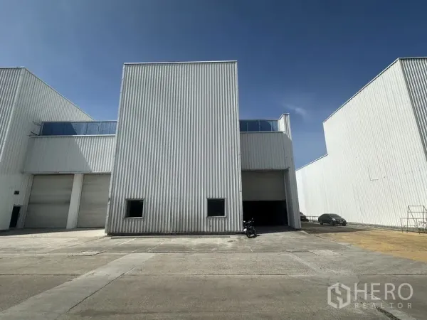 工厂 出租在Khlong Luang, Pathum Thani - 白色金属板厂房立面，宽阔车道与卷闸门，晴朗蓝天。