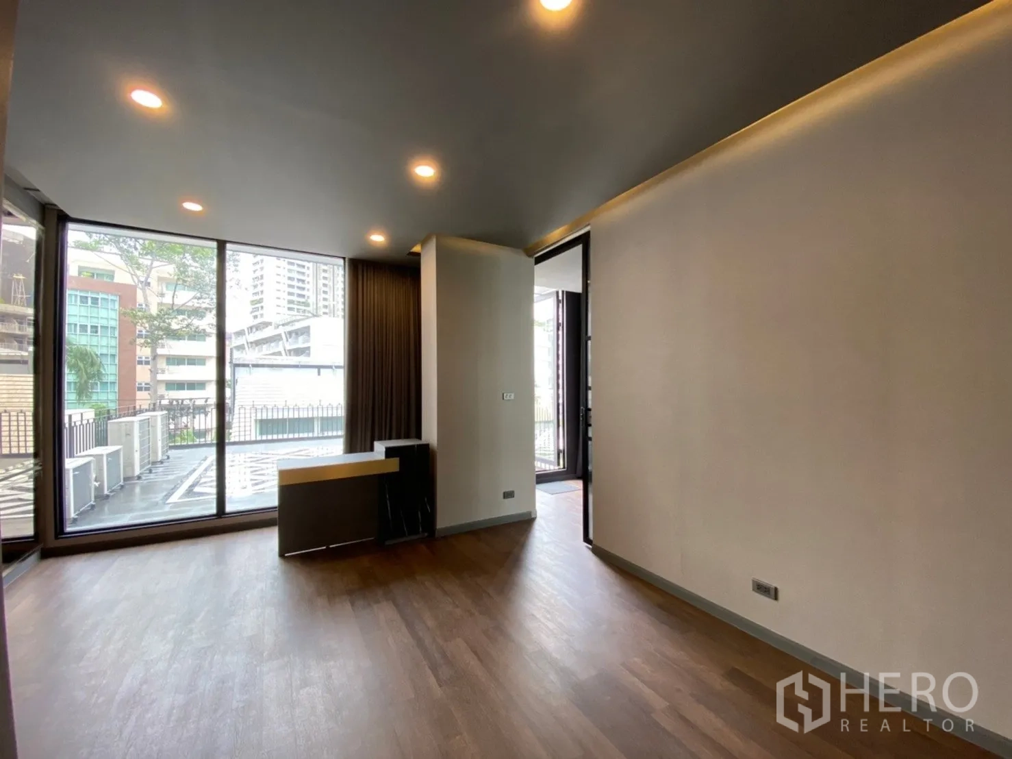 Home Office for rent or sale in Watthana, Bangkok - Corner office with wood floors and sliding doors to a terrace overlooking nearby buildings.