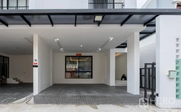 Home Office for rent in Khlong Toei, Bangkok - Covered carport with tiled driveway, secure gate and modern white facade.