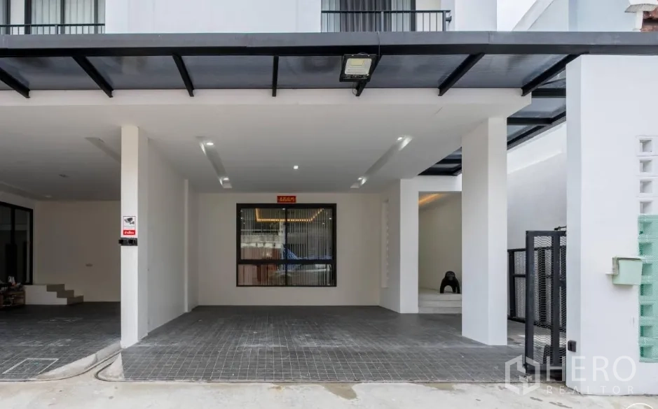 Home Office for rent in Khlong Toei, Bangkok - Covered carport with tiled driveway, secure gate and modern white facade.