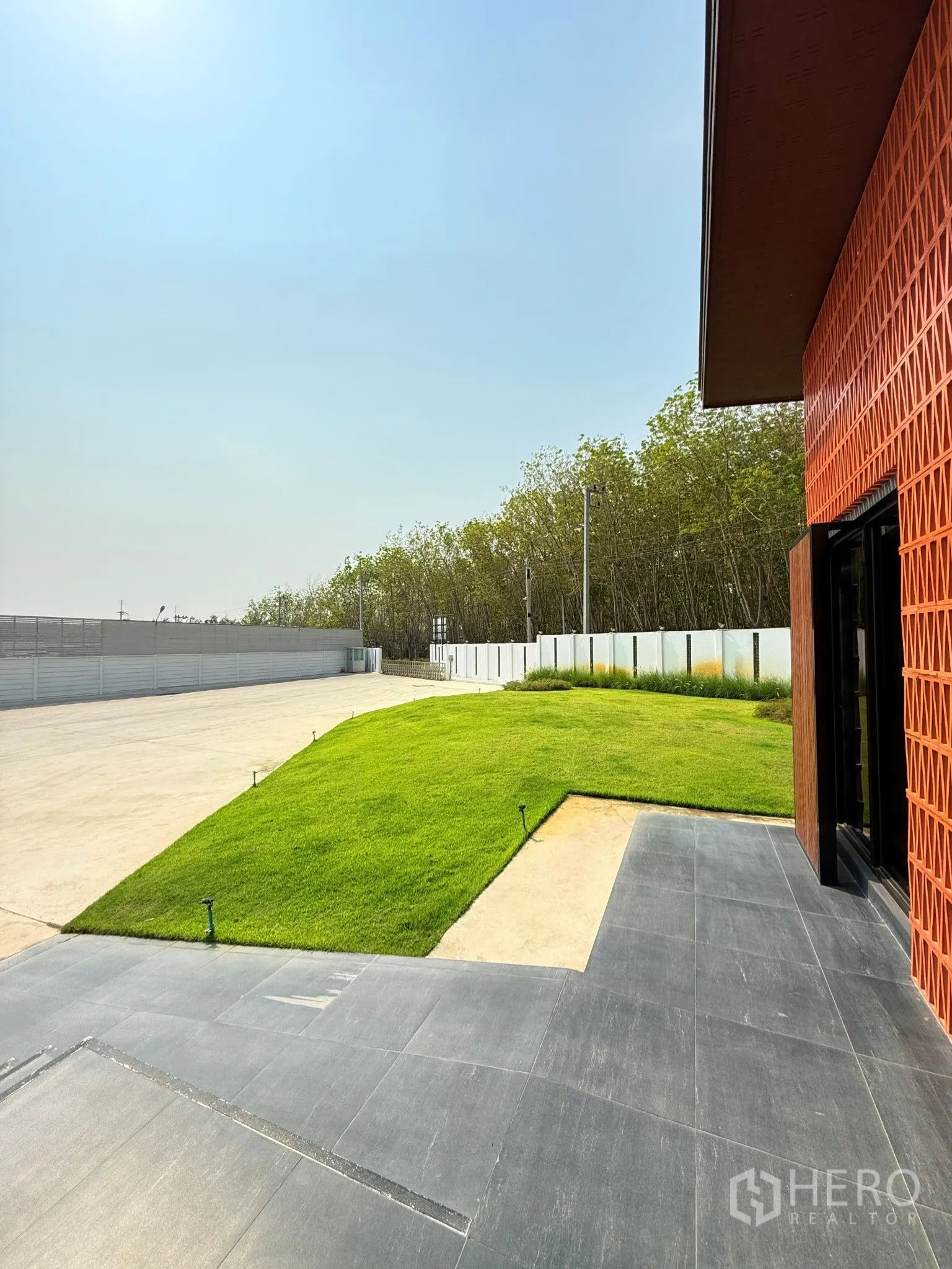 Factory for sale in Ban Bueng, Chon Buri - Green landscaped lawn beside the office building with paved terrace and boundary fence.