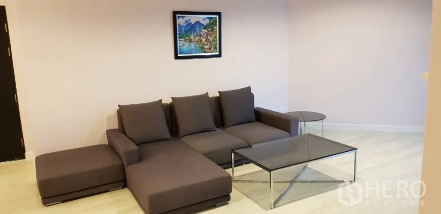 Condominium for rent in Huai Khwang, Bangkok - Bright living room with a gray L-shaped sofa, glass coffee table and light wood flooring.