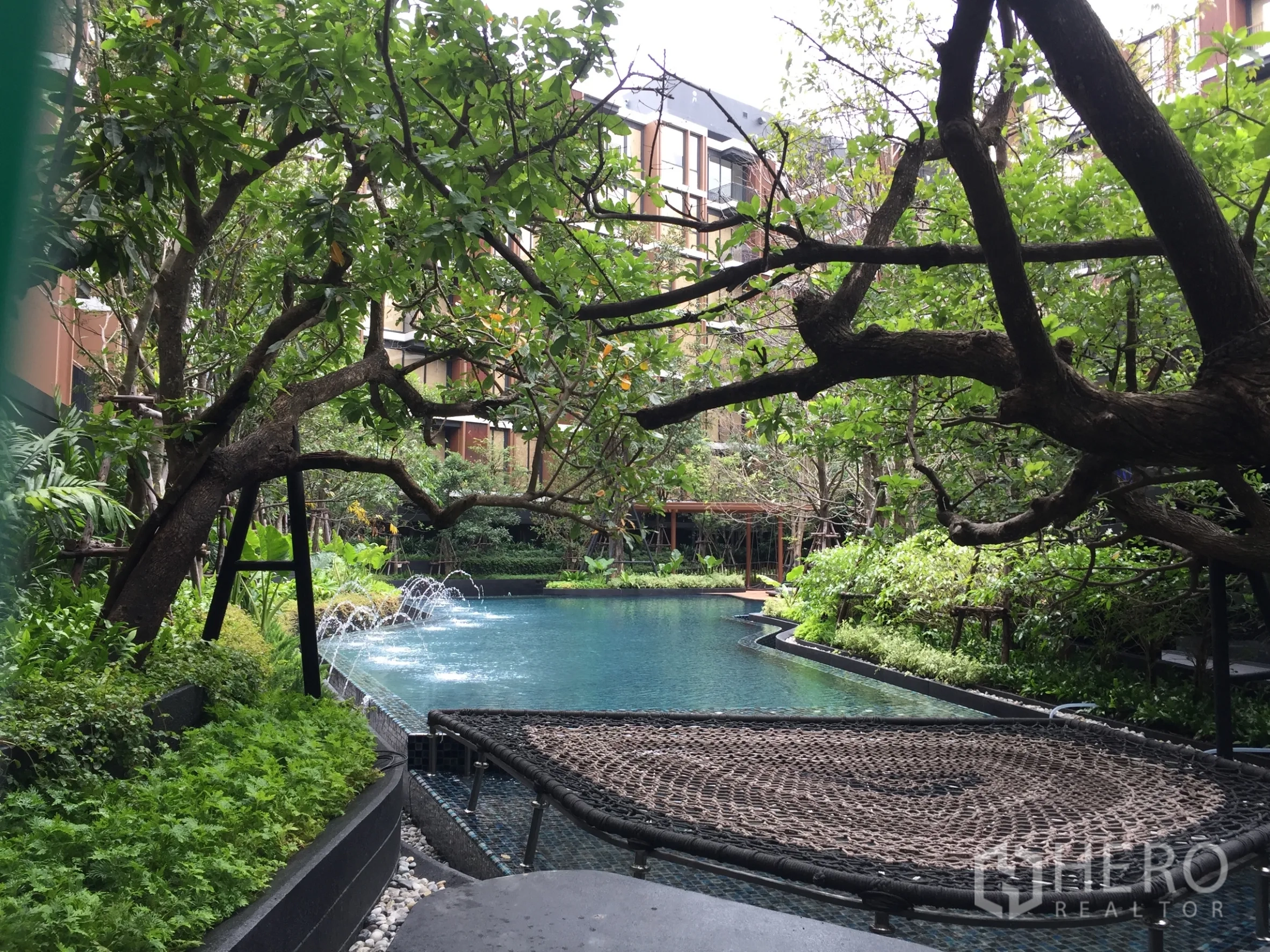 Condominium for rent in Watthana, Bangkok - Resort-style swimming pool in a lush garden setting with fountains and shaded lounging net.