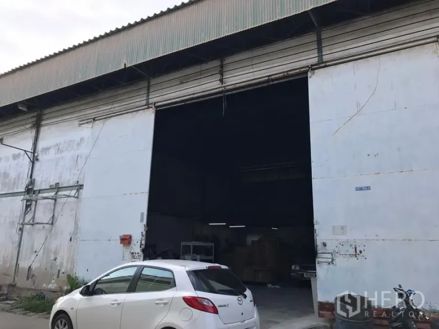 Warehouse for rent in Bang Phli, Samut Prakan - Industrial warehouse facade with extra-wide steel shutter door, high-clearance entrance and on-site parking area.