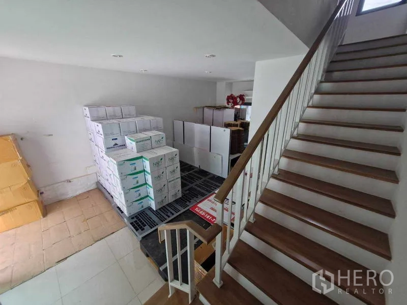 联排别墅 出售在Phra Pradaeng, Samut Prakan - 一层客厅空间与楼梯，室内堆放纸箱，地砖与木地板