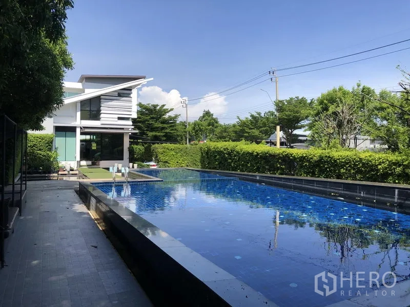 Detached House for rent in Saphan Sung, Bangkok - Communal swimming pool with modern clubhouse and hedge-lined deck.