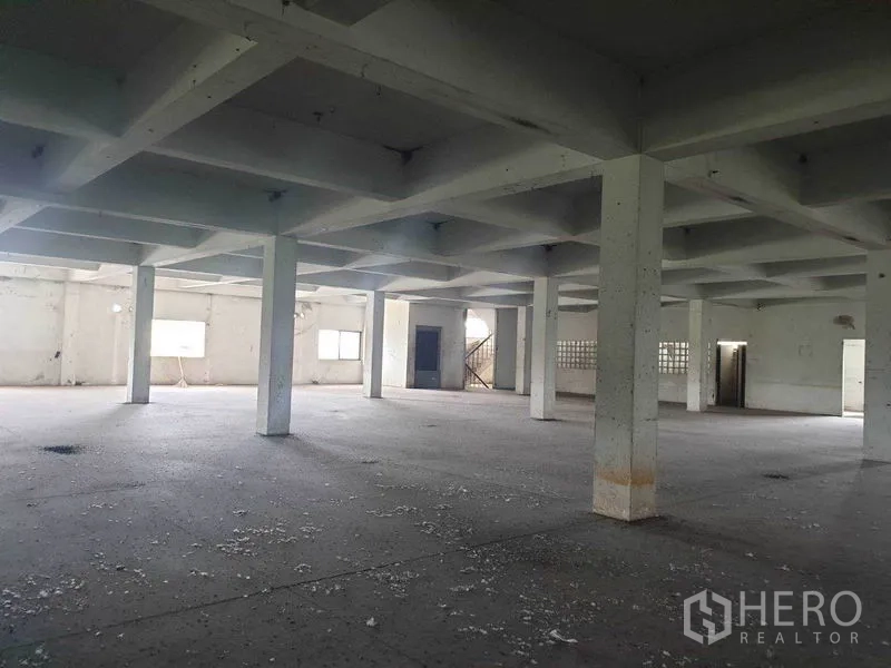 Shophouse for rent in Bang Bo, Samut Prakan - Spacious open-plan interior with concrete floor, grid ceiling and square columns in an empty shophouse level.